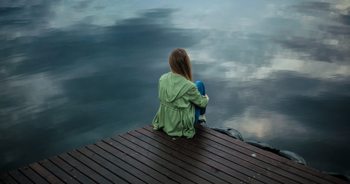 Frau sitzt einsam auf einem Steg am See
