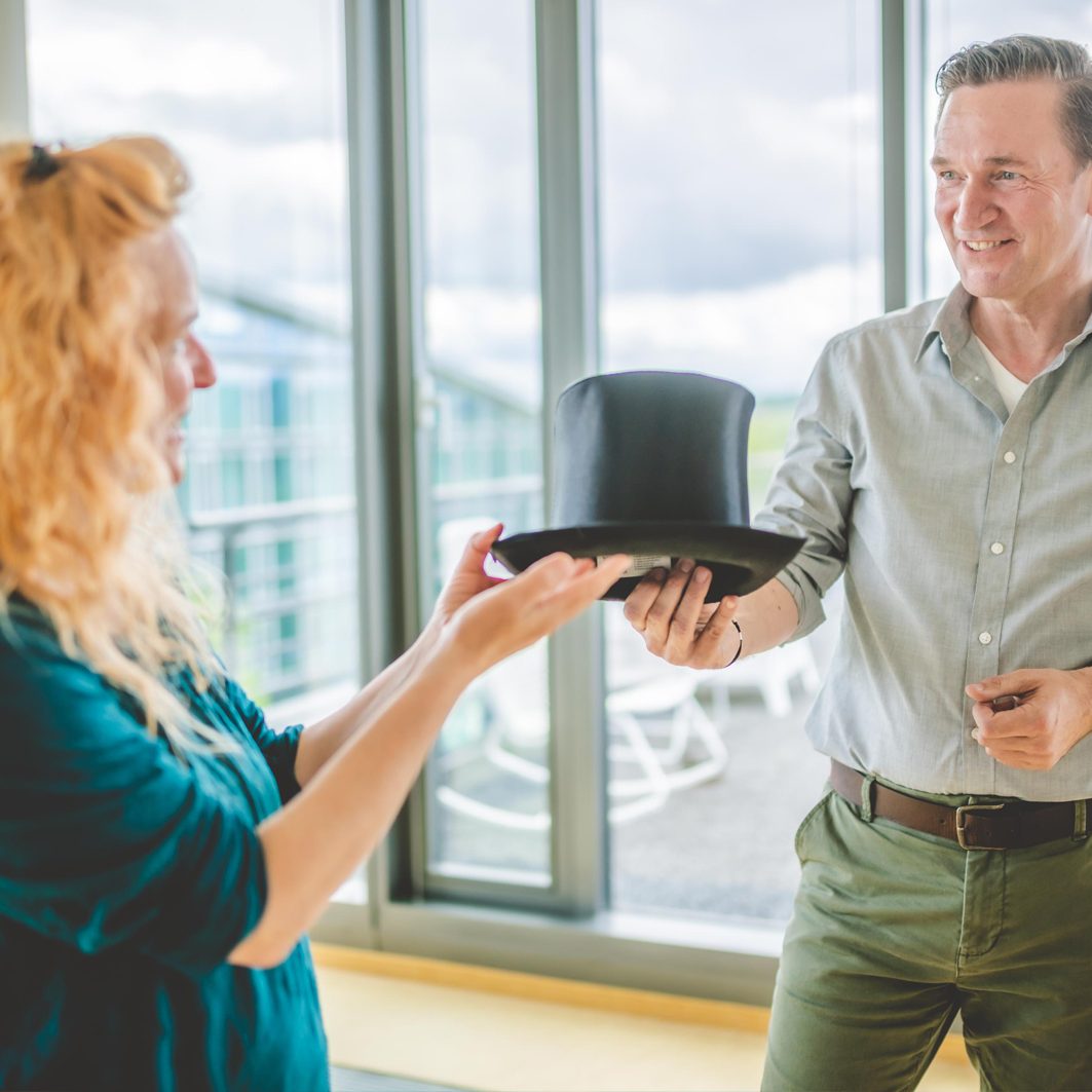 Eine Frau reicht einem Mann einen Zylinder als Requisite