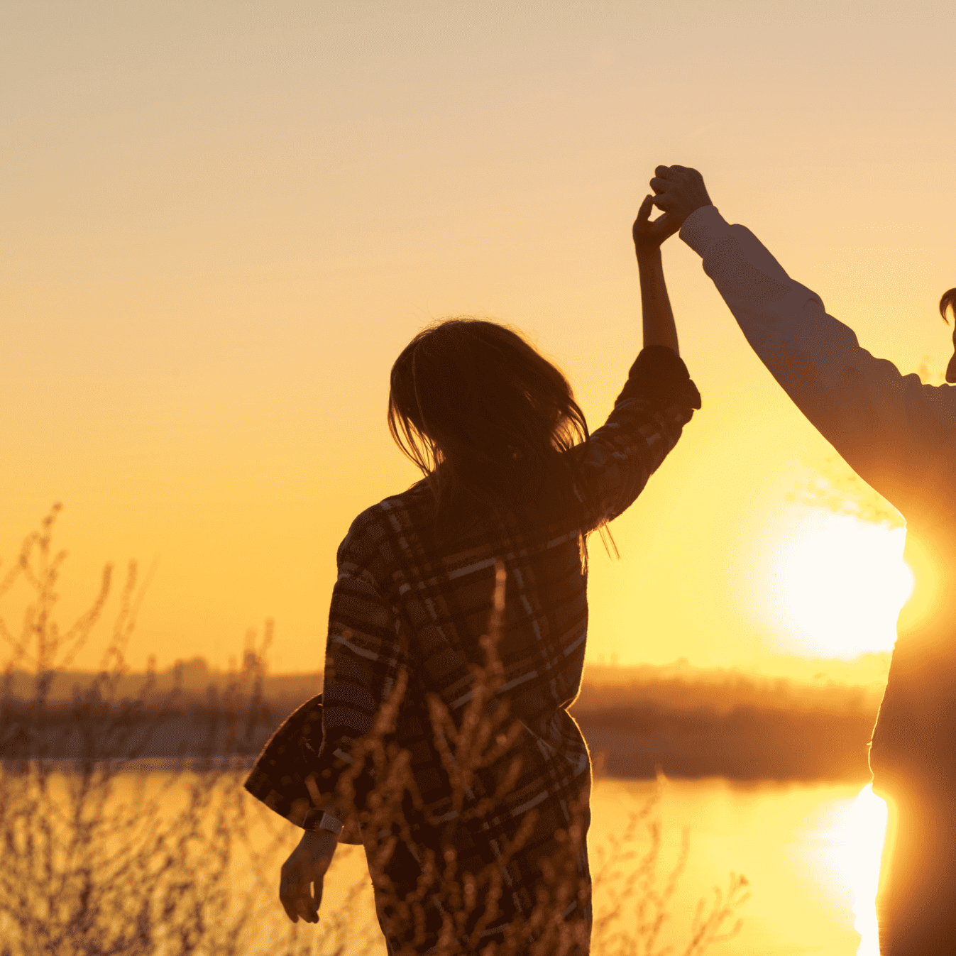 Zwei Personen halten gemeinsam die Hände hoch während eines Sonnenaufgangs