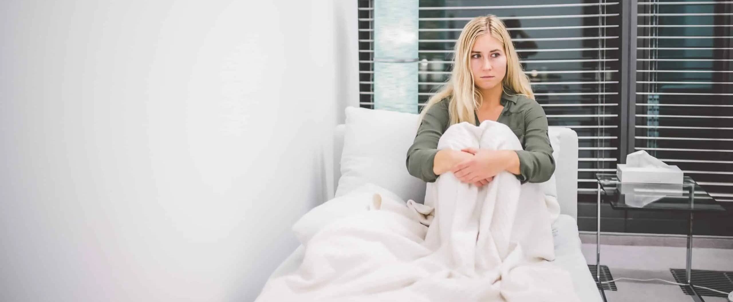 Eine Frau sitzt mit angezogenen Beinen auf einem Bett