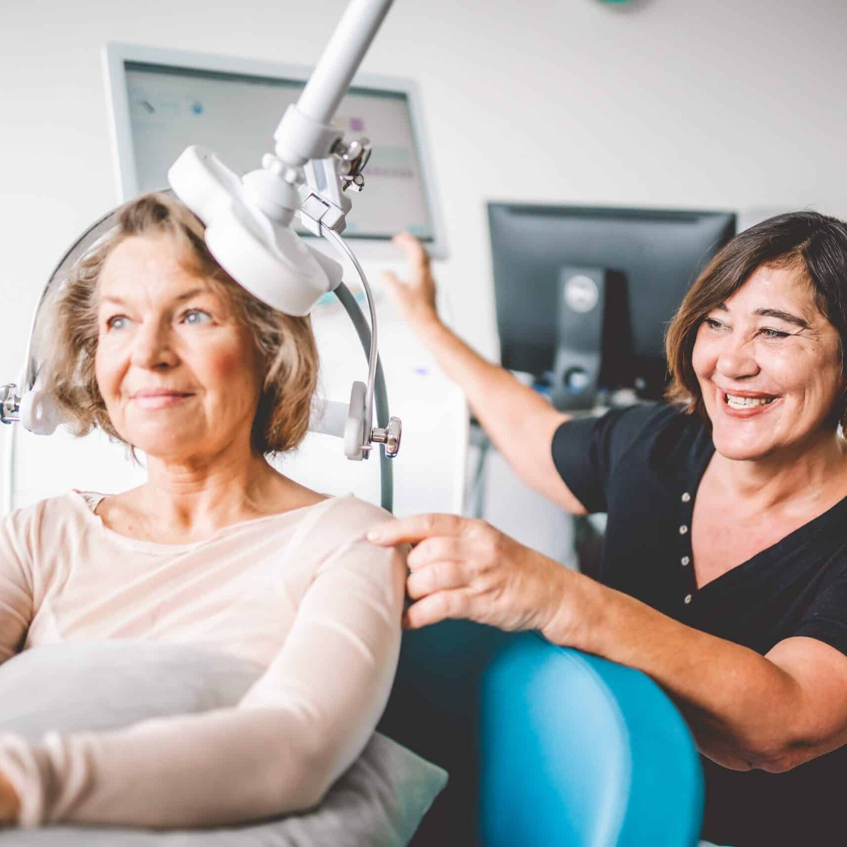 Eine Frau erhält die rTMS Therapie; dafür sitzt sie auf einem Stuhl unter dem Gerät