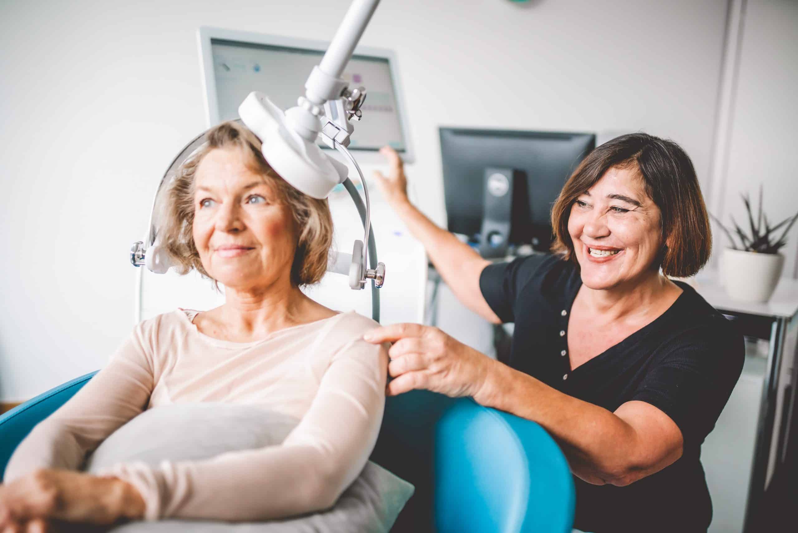 Eine Frau erhält die rTMS Therapie; dafür sitzt sie auf einem Stuhl unter dem Gerät