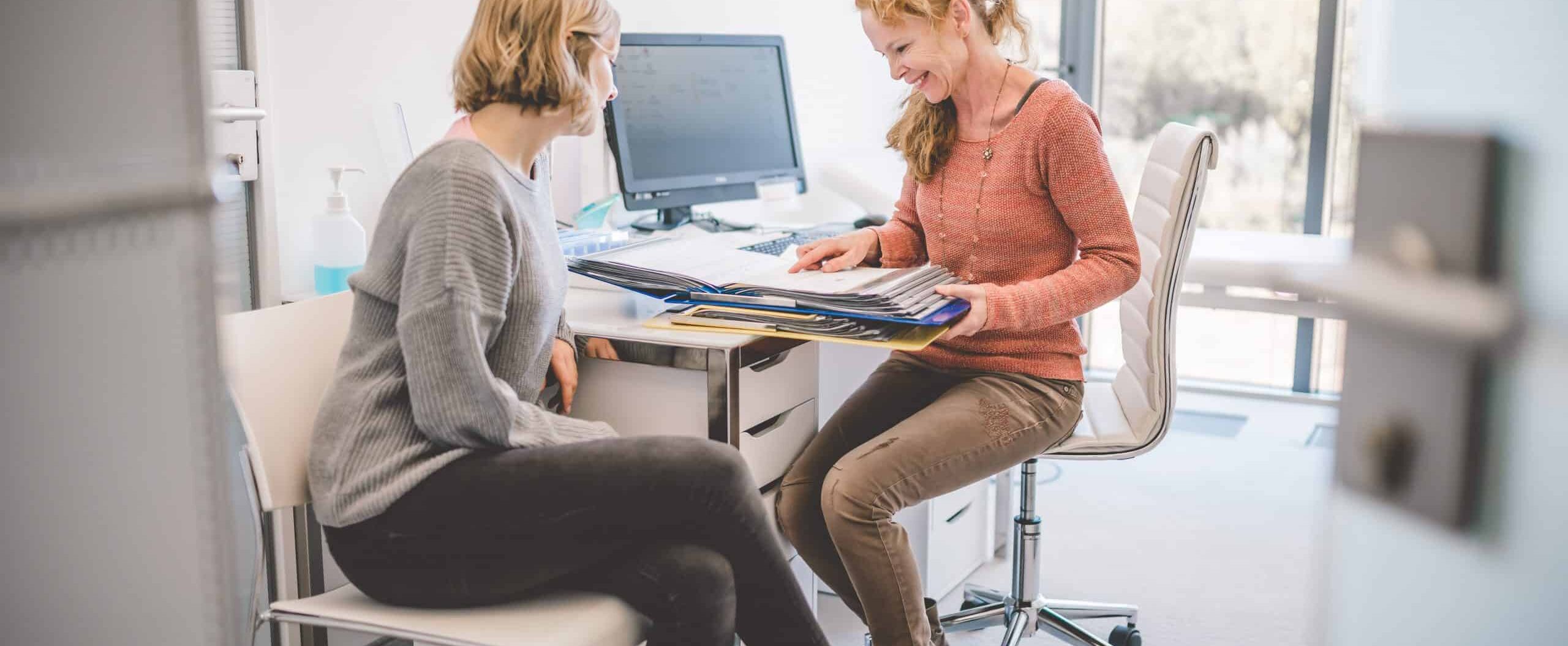 eine Therapeutin und eine Patientin sitzen gemeinsam an einem Tisch und sprechen über die Patientenakte