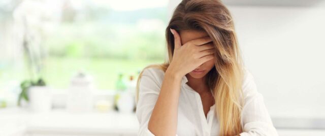 Migräne behandeln Eine Frau fasst sich an den Kopf, weil sie Schmerzen hat