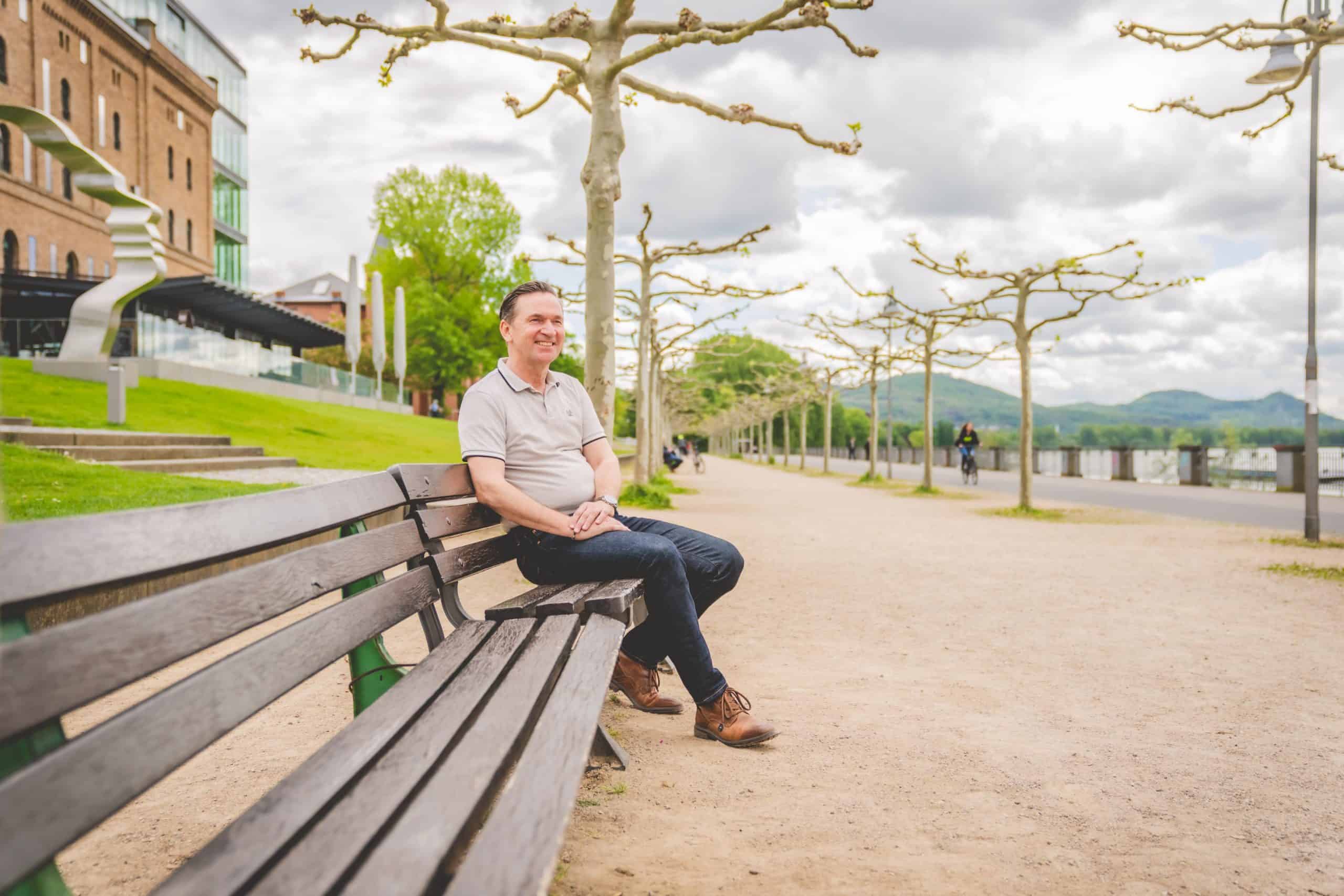 Ein Mann sitzt auf einer Bank draußen und lächelt entspannt