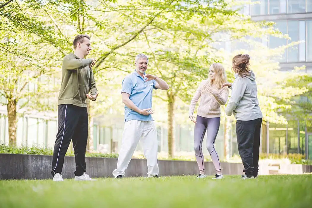 Gruppe von Menschen macht Bewegungsübungen im Freien vor der Betagenese Klinik, während sie Körpertherapien und Physiotherapie erhalten.