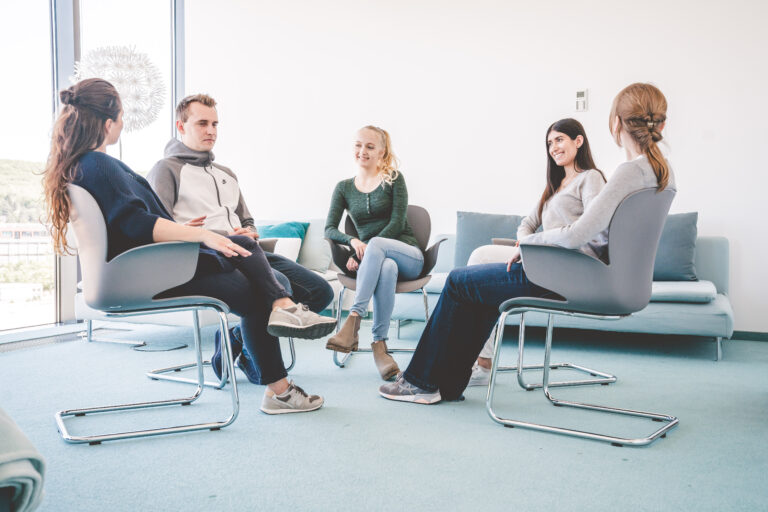 Jugendliche sitzen gemeinsam im Stuhlkreis während einer Gruppentherapie Sitzung und unterhalten sich miteinander.