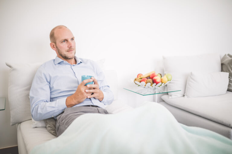 Patient sitzt bequem im Bett mit einem Getränk in der Hand.