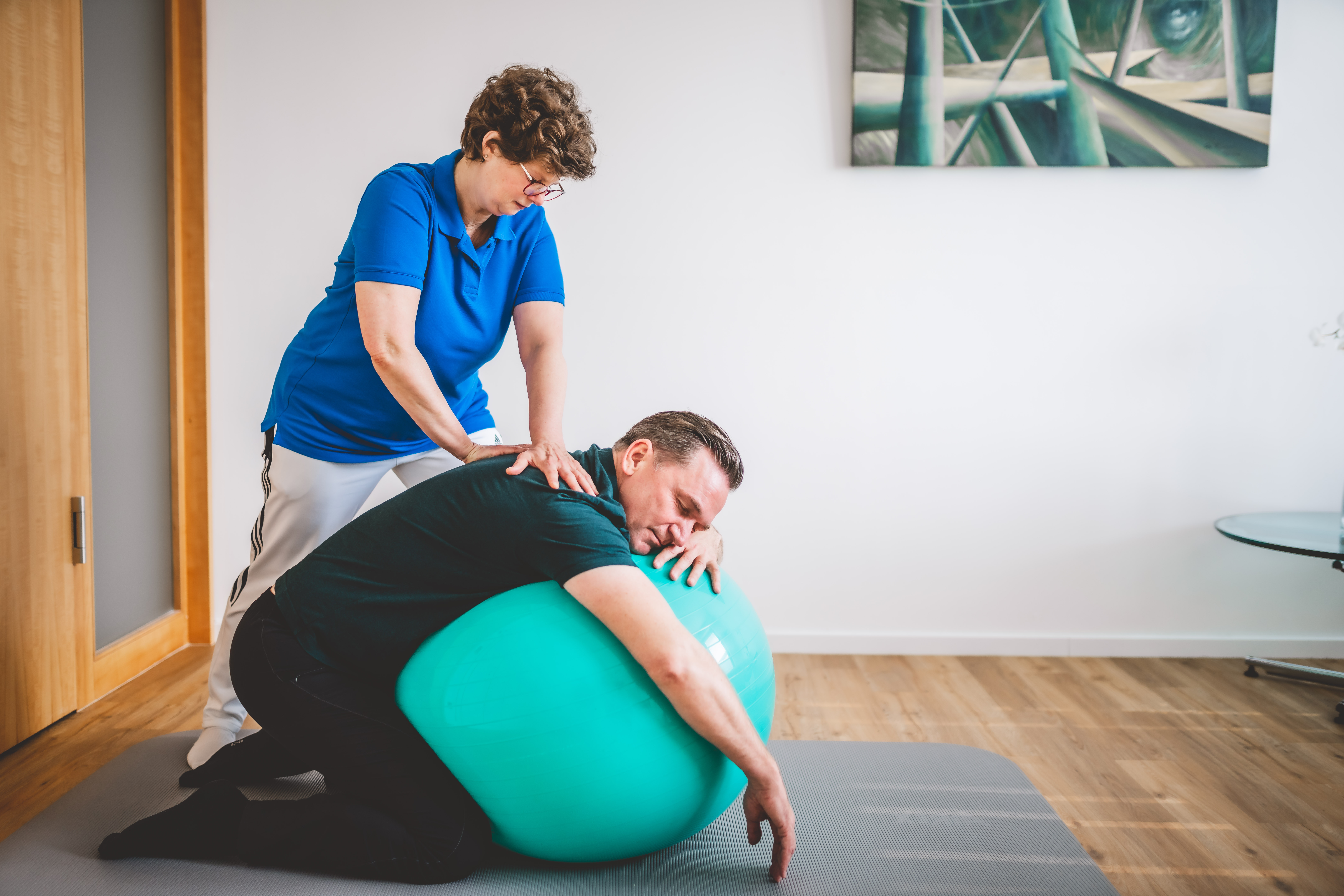 Physiotherapeutin behandelt einen Patienten während er auf einem Gymnastikball liegt