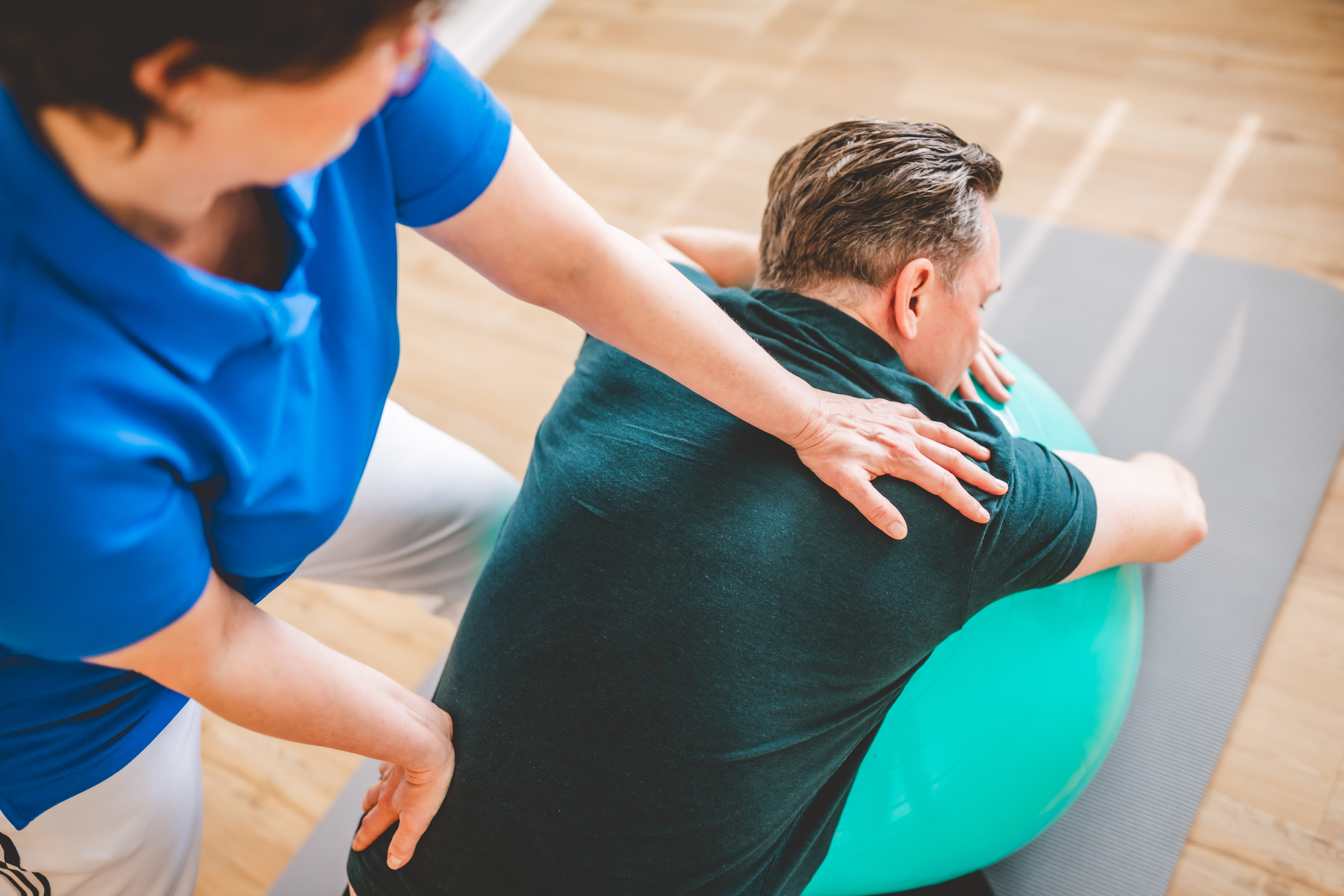 Physiotherapie mit einem Patienten auf einem Gymnastikball.