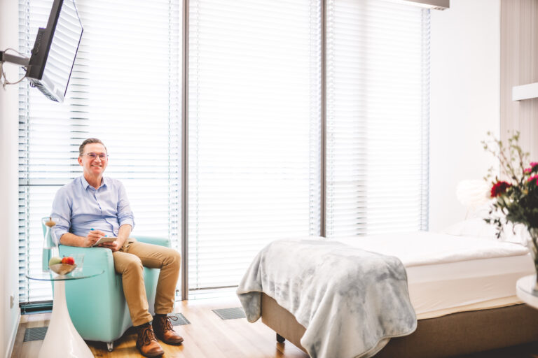 Helles und freundliches Patientenzimmer der BetaGenese Klinik mit männlichen Patient im Sessel.