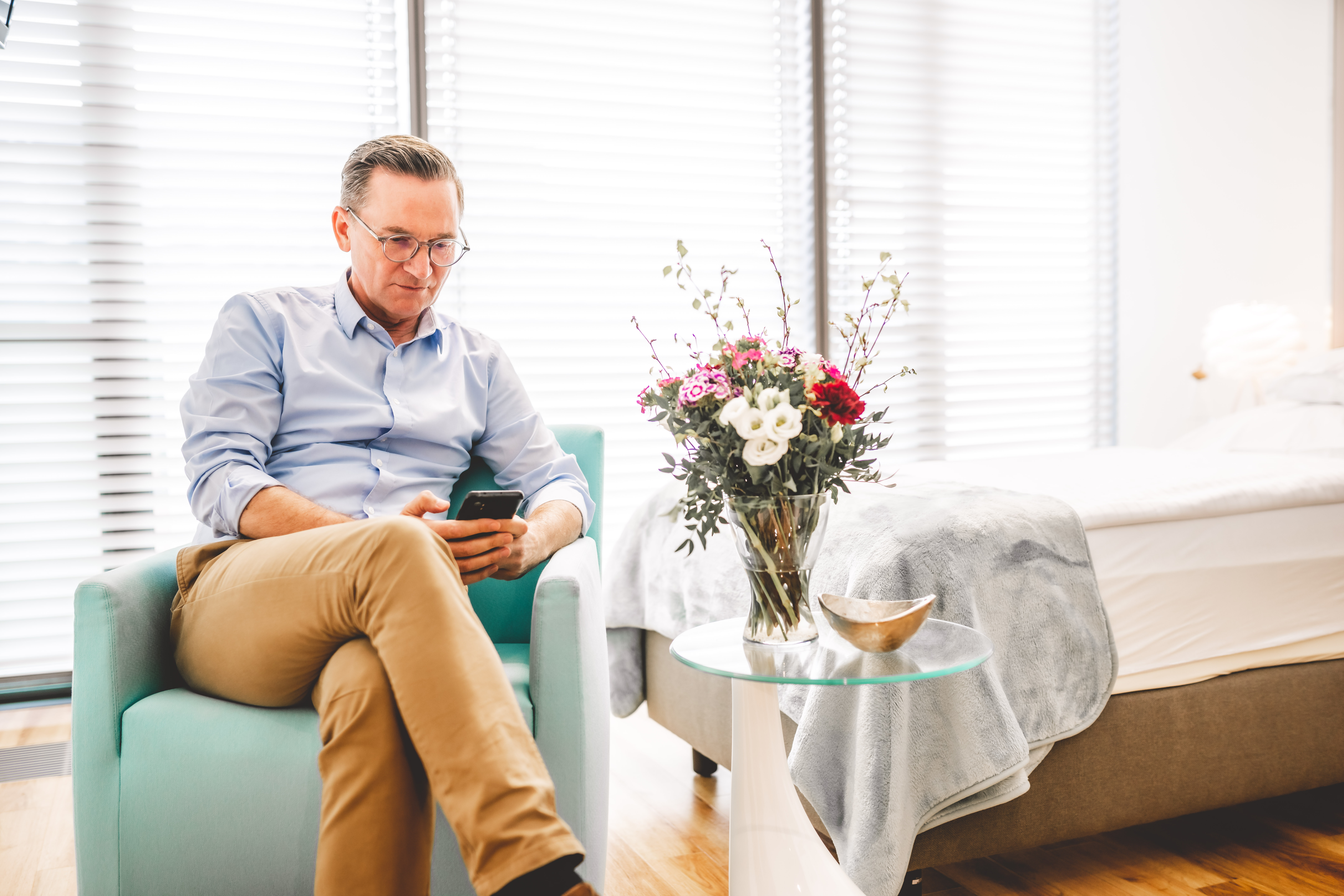 Nahaufnahme eines Patienten der auf einem Sessel im Patientenzimmer sitzt und sein Handy ließt.