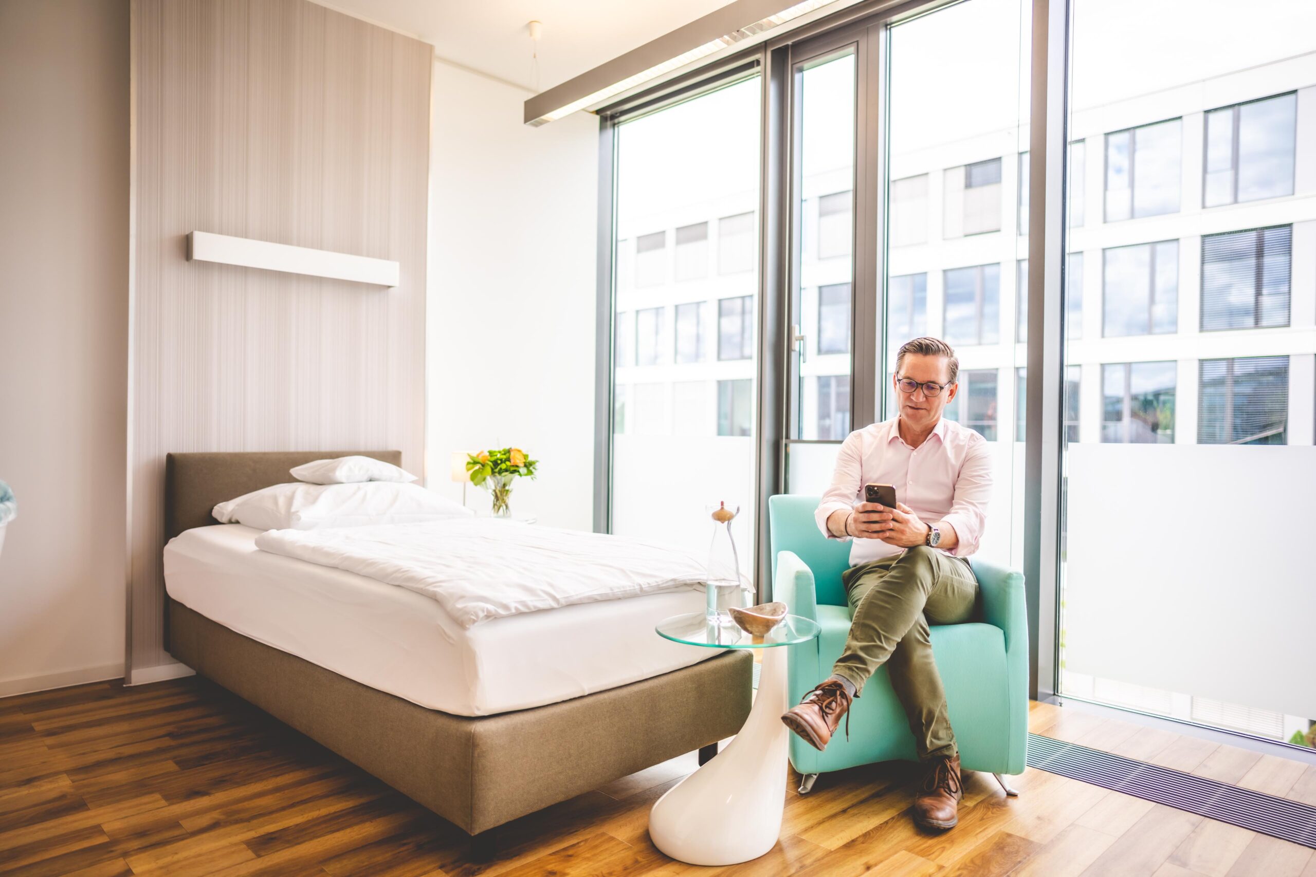 Mann sitzt am Handy in einem hellen und freundlichen Patientenzimmer.