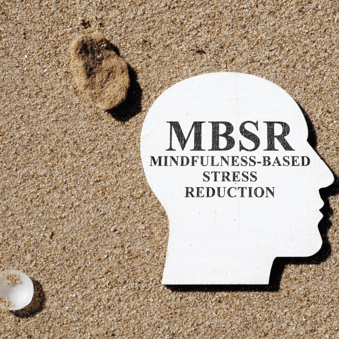 Holzfigur eines Kopfes mit der Aufschrift MBSR – Mindfulness-Based Stress Reduction im Sand